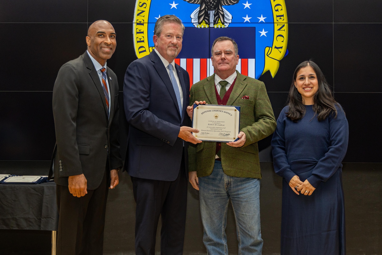 People stand indoors on a stage holding a certificate.