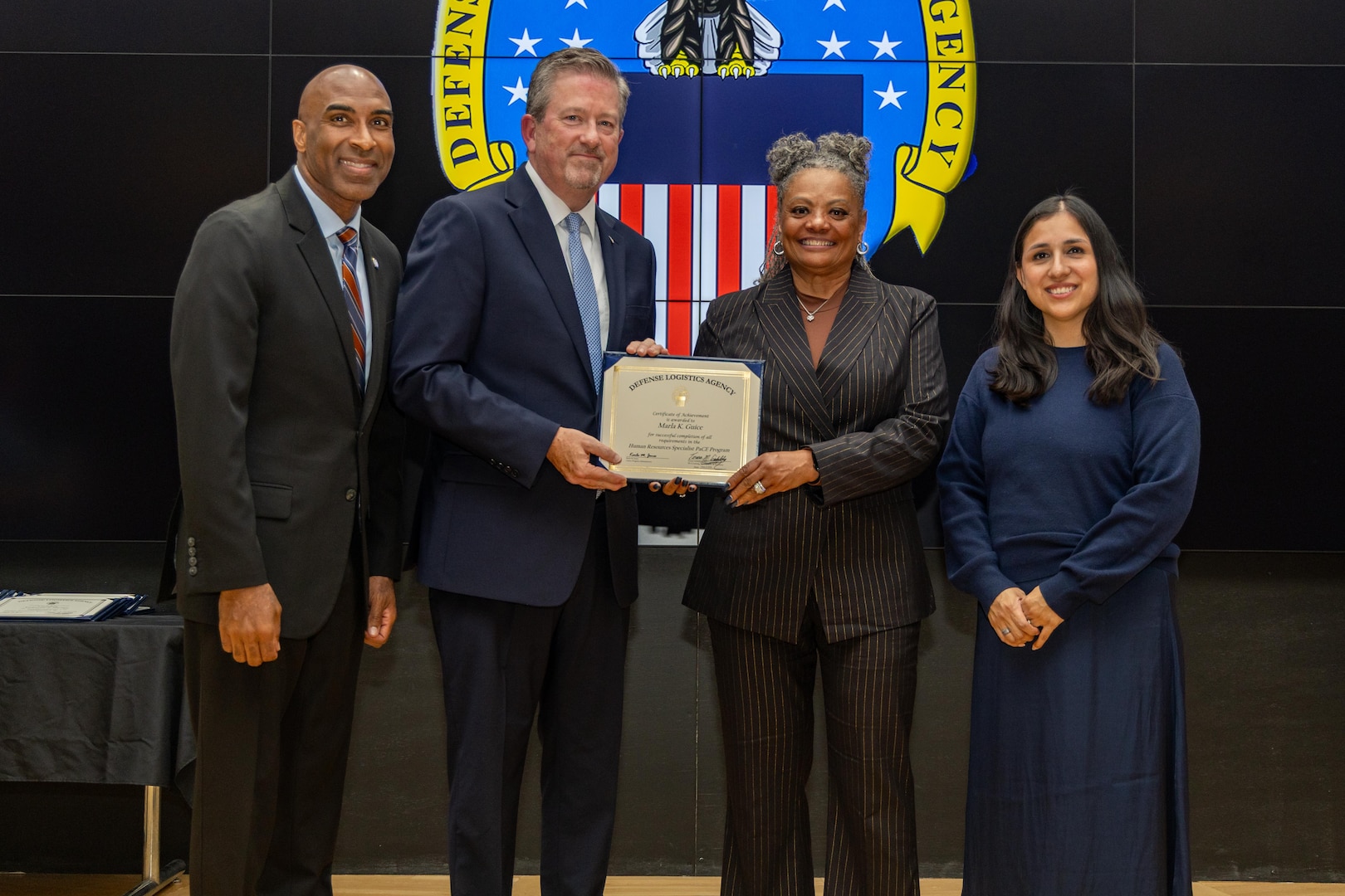 People stand indoors on a stage holding a certificate.