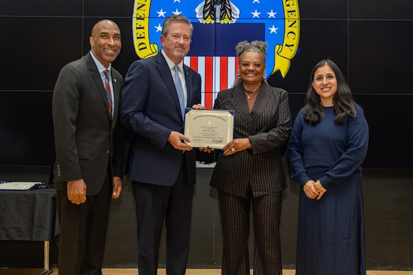 People stand indoors on a stage holding a certificate.