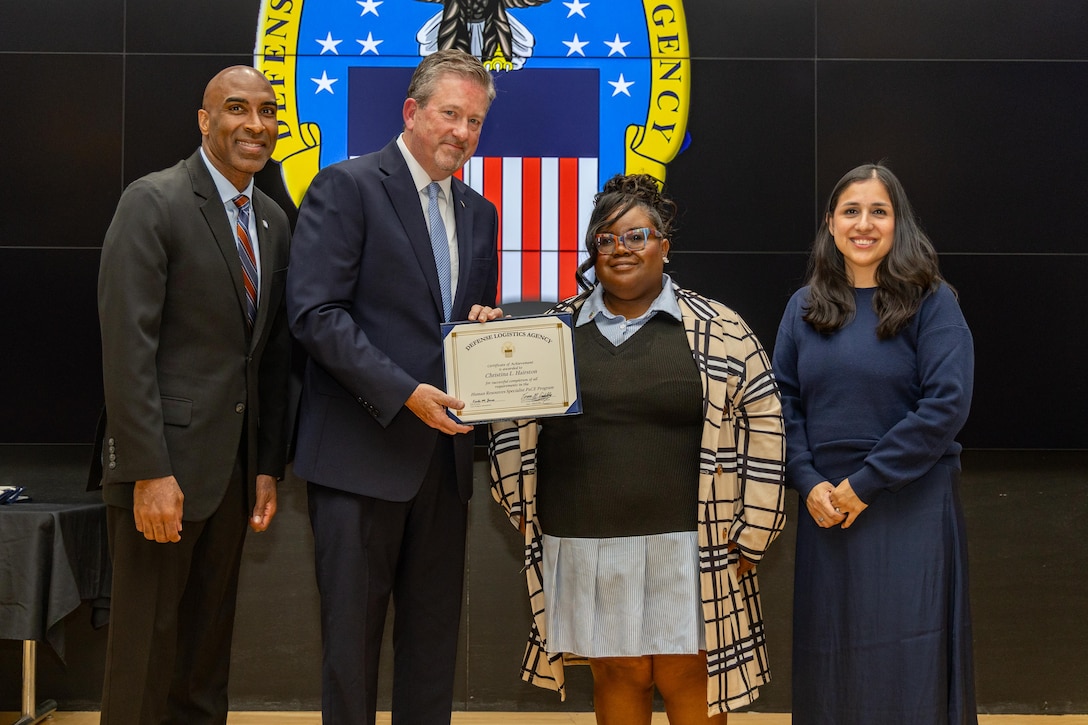 People stand indoors on a stage holding a certificate.