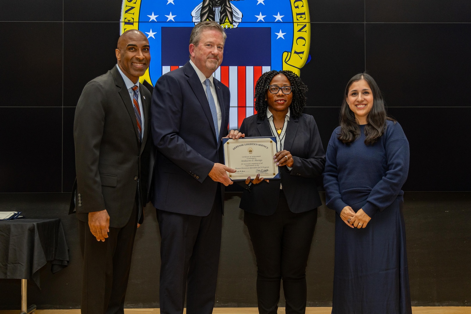 People stand indoors on a stage holding a certificate.