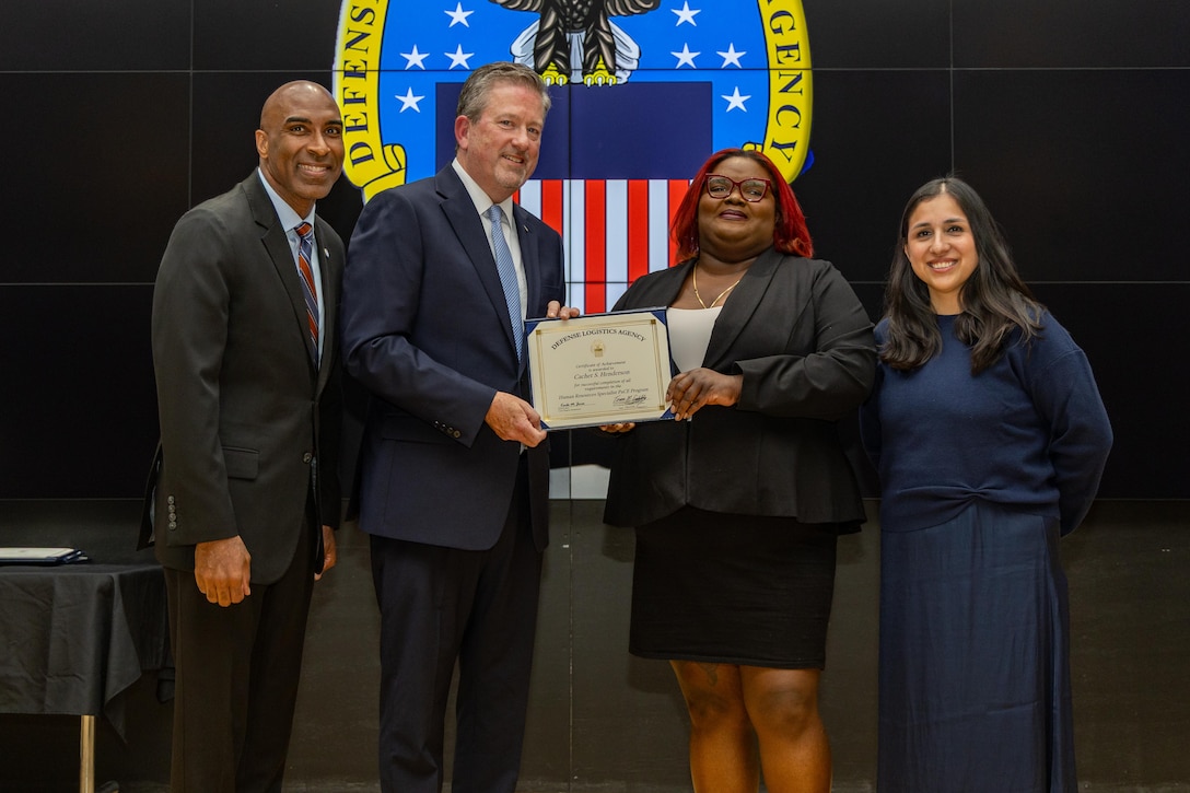 People stand indoors on a stage holding a certificate.