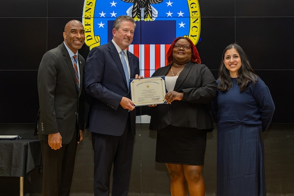 People stand indoors on a stage holding a certificate.