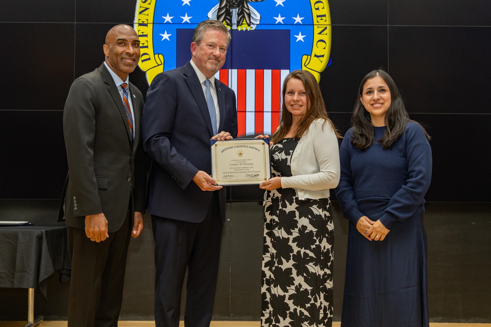 People stand indoors on a stage holding a certificate.