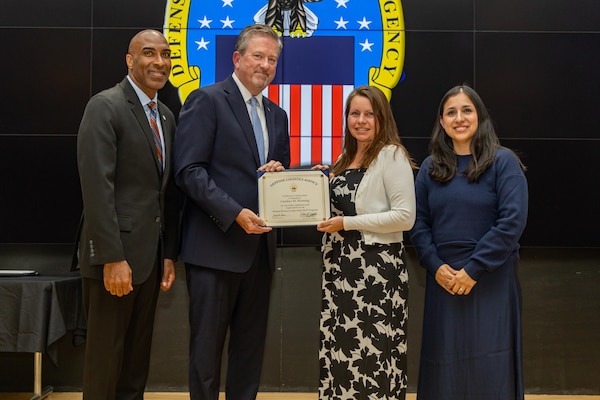 People stand indoors on a stage holding a certificate.