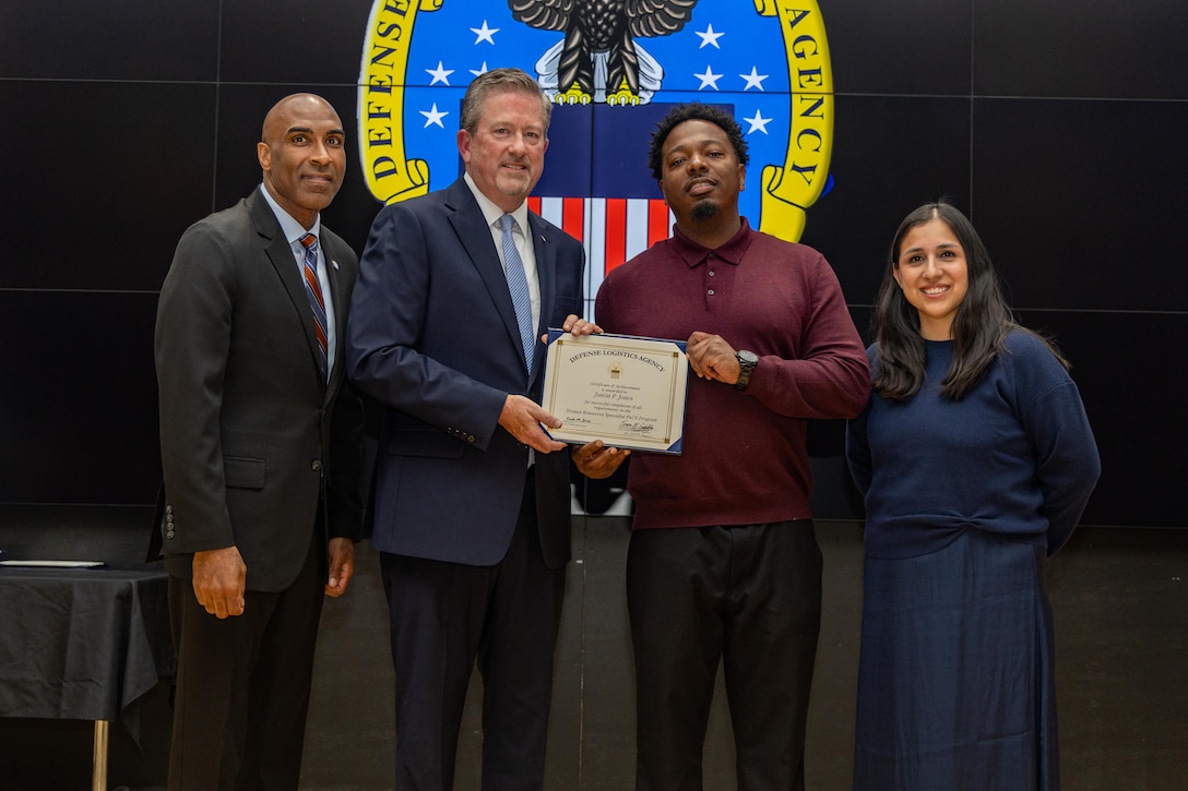 People stand indoors on a stage holding a certificate.