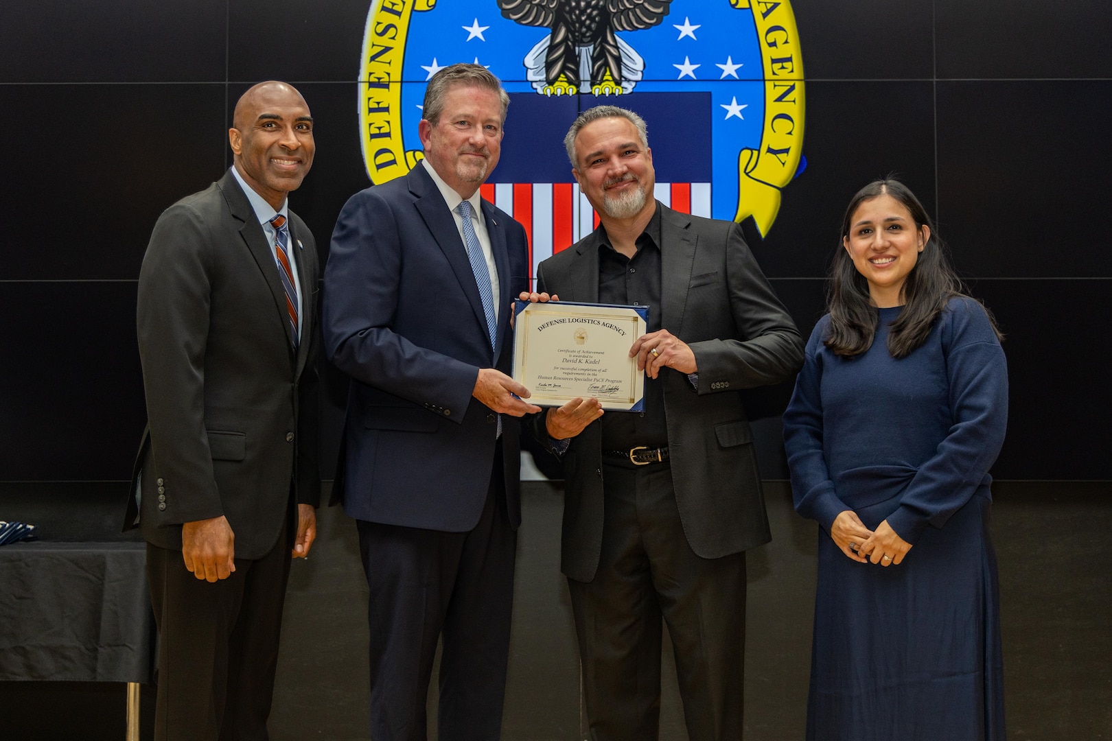 People stand indoors on a stage holding a certificate.