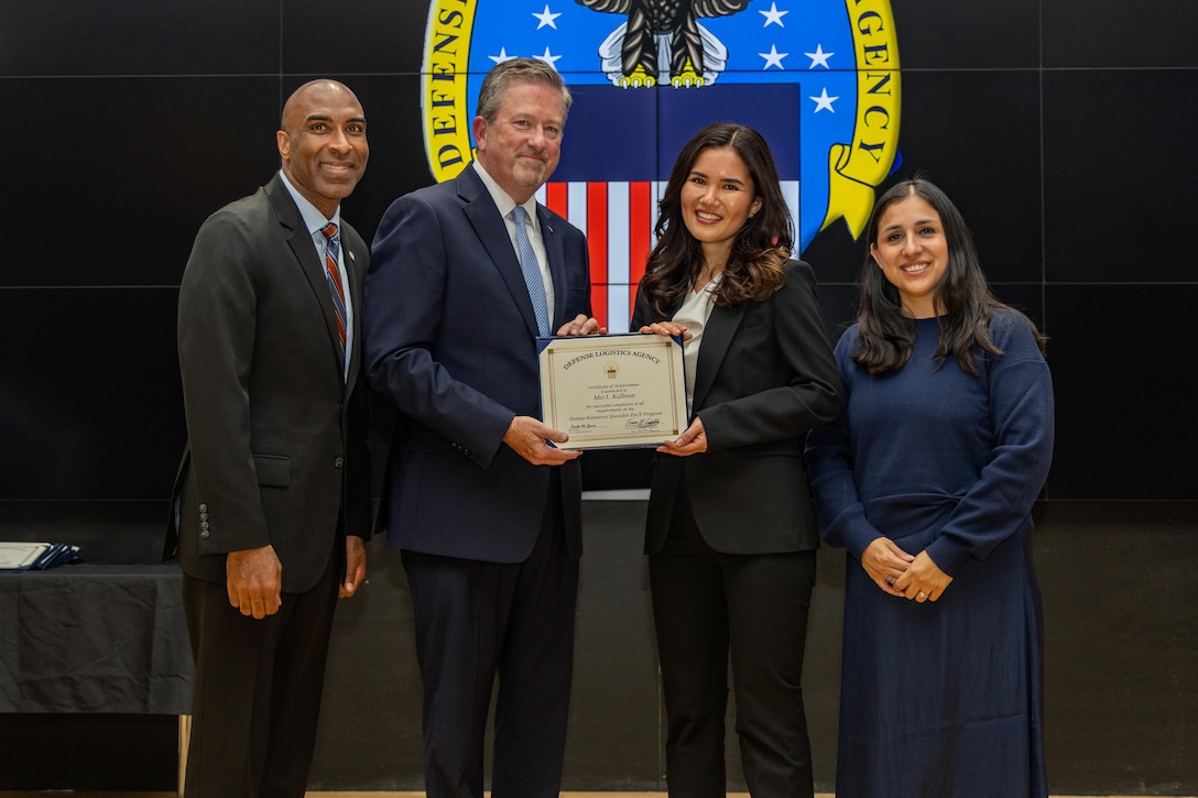 People stand indoors on a stage holding a certificate.