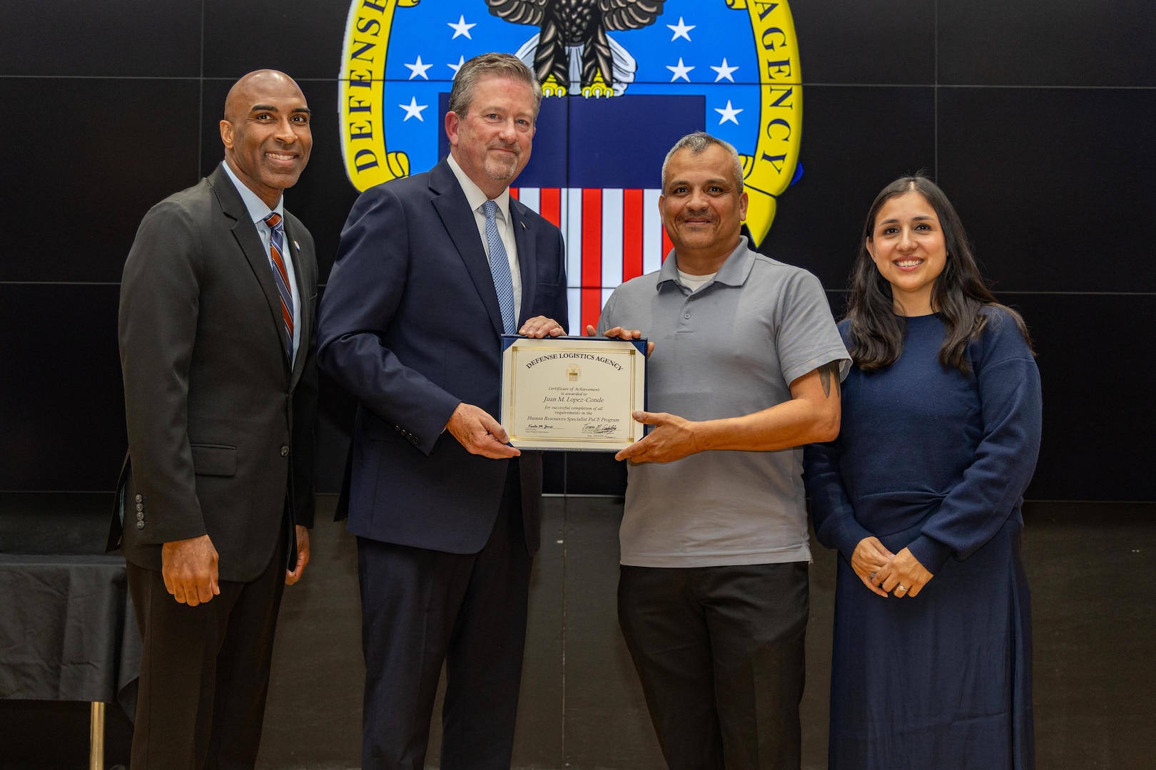 People stand indoors on a stage holding a certificate.