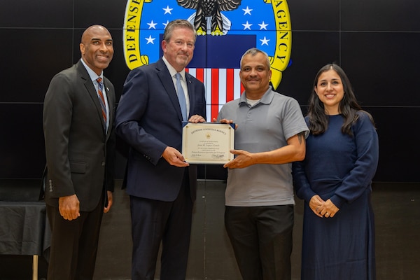 People stand indoors on a stage holding a certificate.