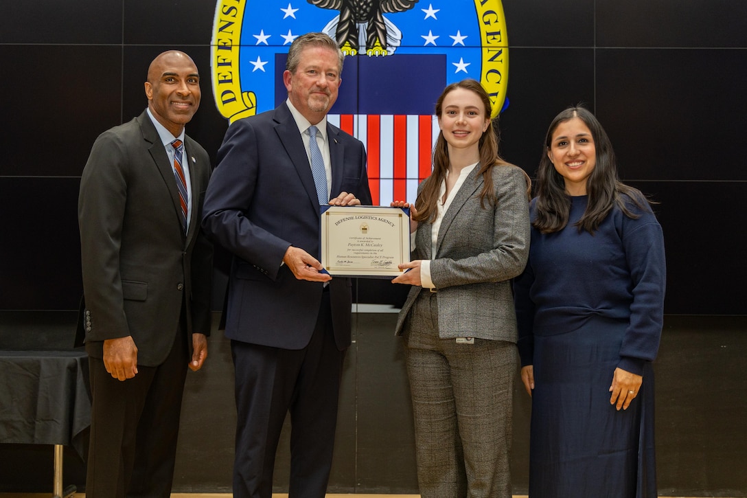 People stand indoors on a stage holding a certificate.