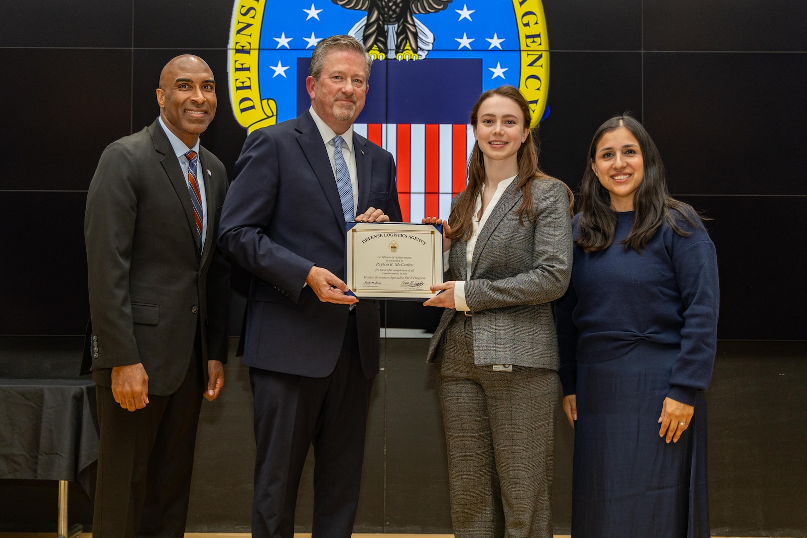 People stand indoors on a stage holding a certificate.
