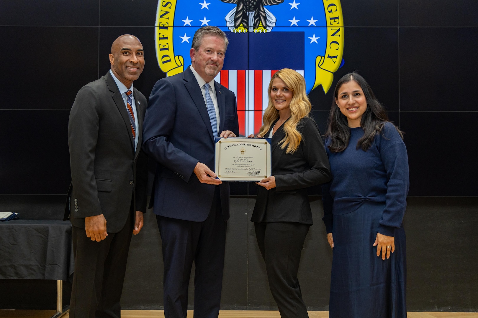 People stand indoors on a stage holding a certificate.