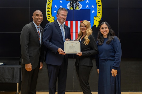 People stand indoors on a stage holding a certificate.