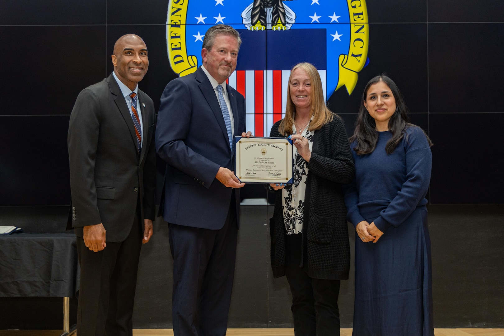 People stand indoors on a stage holding a certificate.