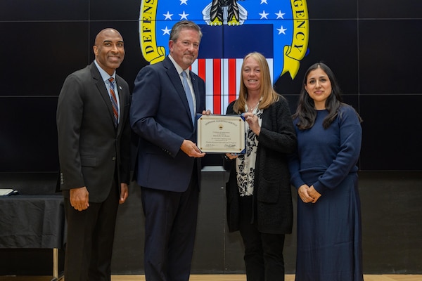 People stand indoors on a stage holding a certificate.