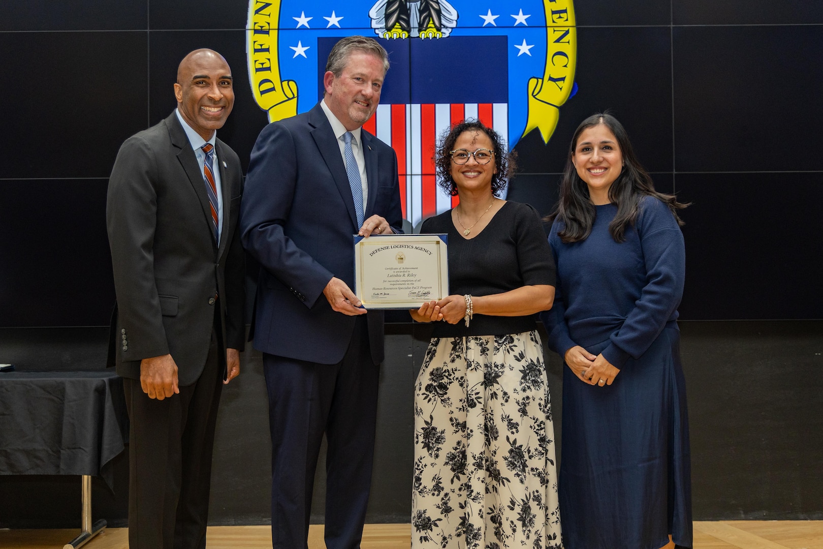 People stand indoors on a stage holding a certificate.