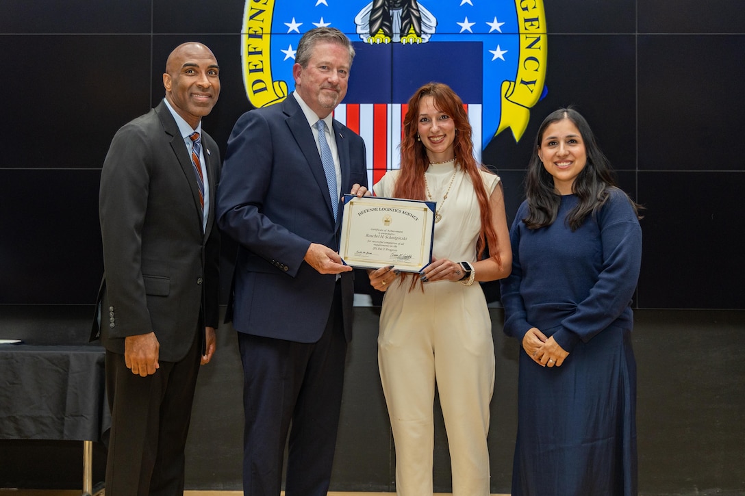 People stand indoors on a stage holding a certificate.