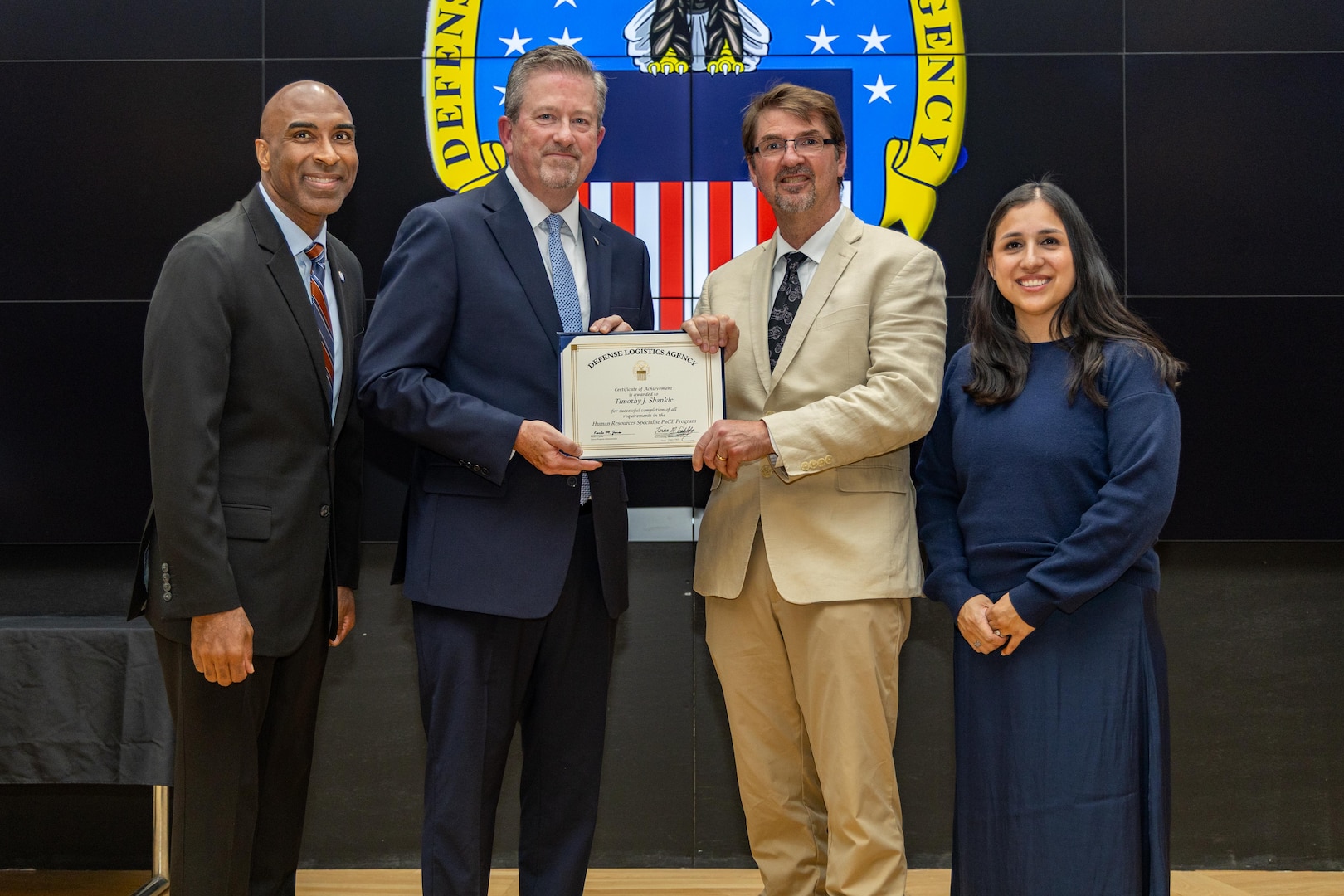 People stand indoors on a stage holding a certificate.