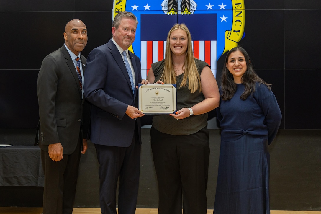 People stand indoors on a stage holding a certificate.