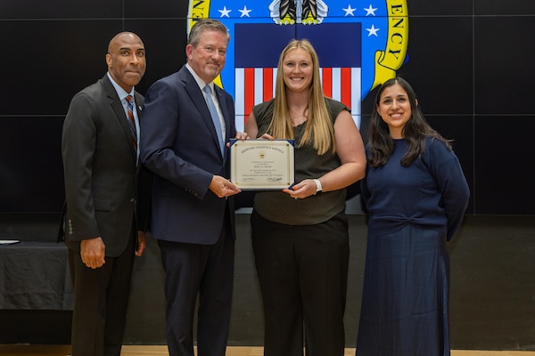 People stand indoors on a stage holding a certificate.