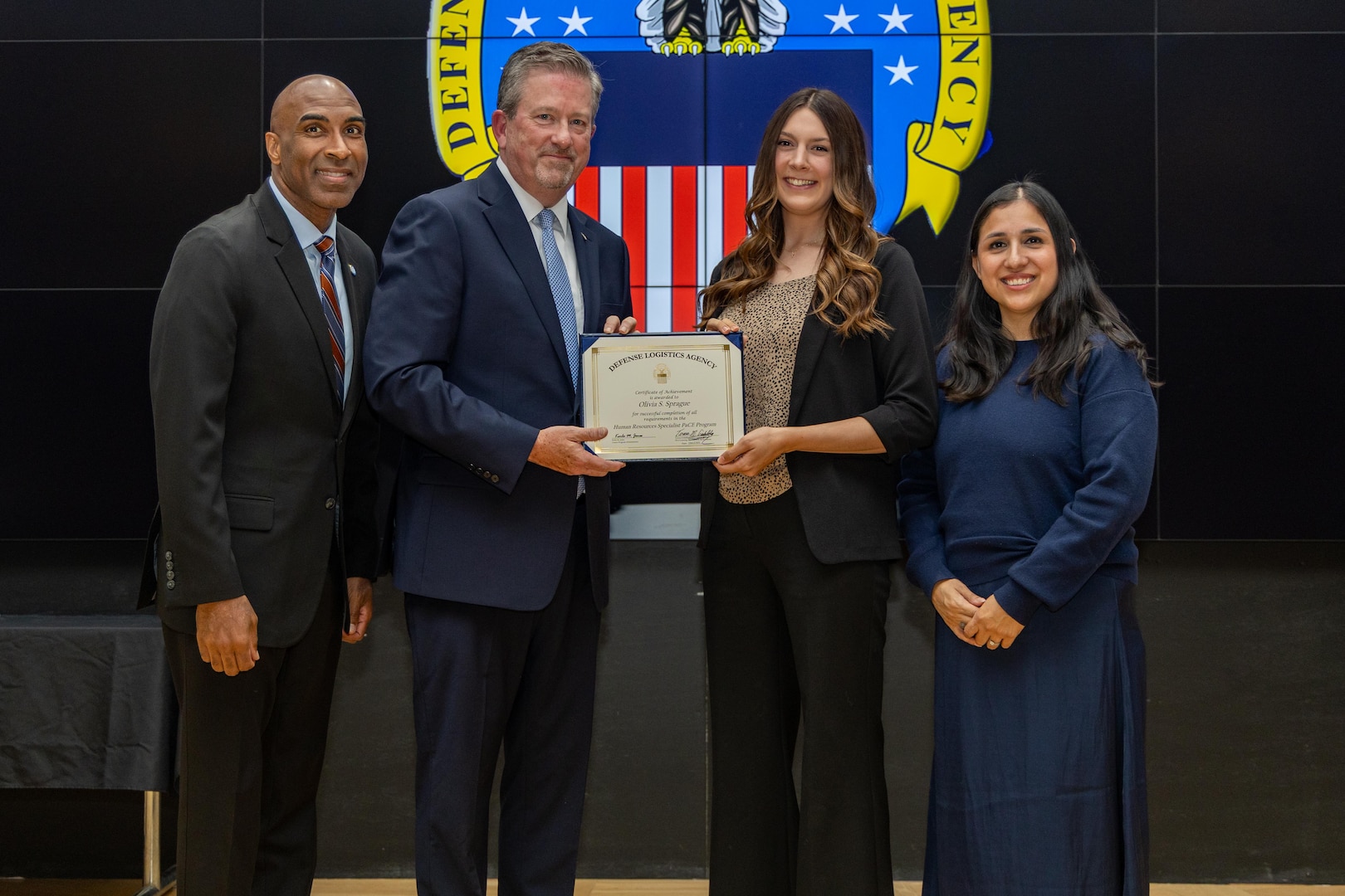 People stand indoors on a stage holding a certificate.