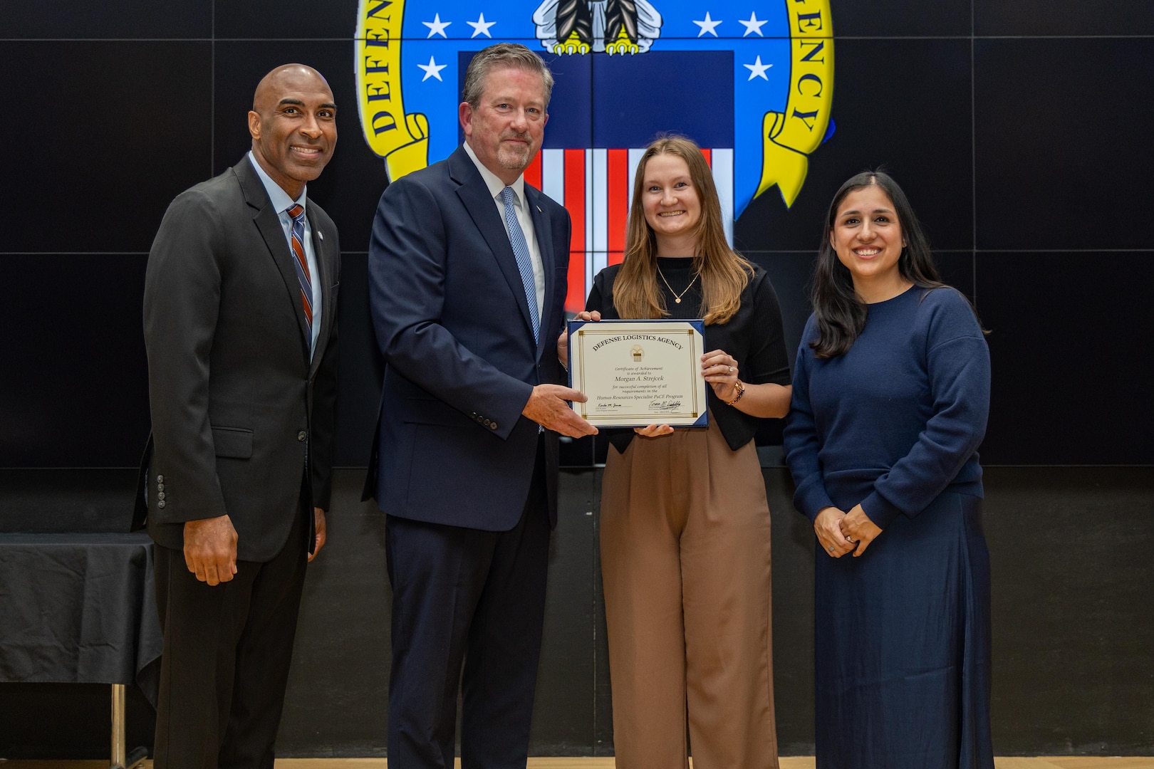 People stand indoors on a stage holding a certificate.