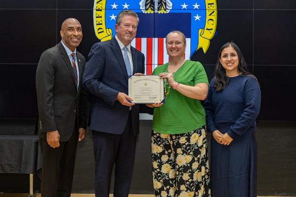 People stand indoors on a stage holding a certificate.