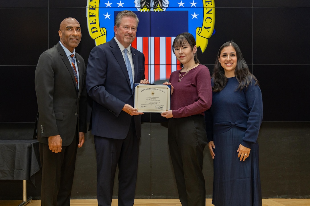 People stand indoors on a stage holding a certificate.