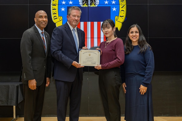 People stand indoors on a stage holding a certificate.
