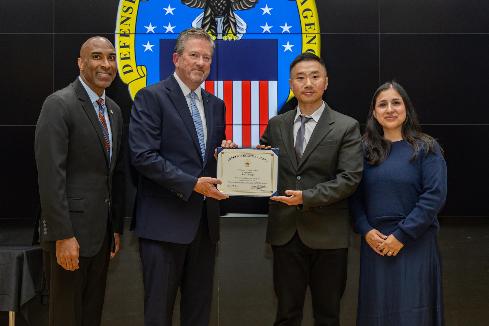 People stand indoors on a stage holding a certificate.