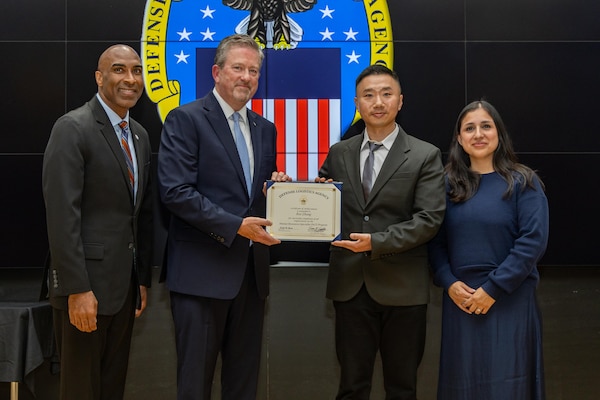 People stand indoors on a stage holding a certificate.