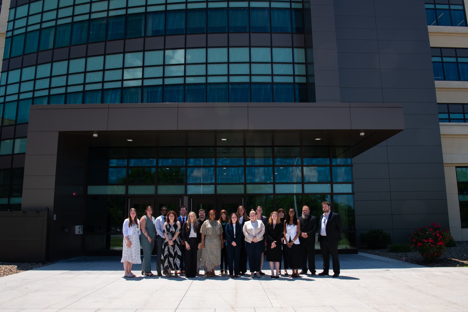 A group of people stand outside in front of a large building on a sunny day