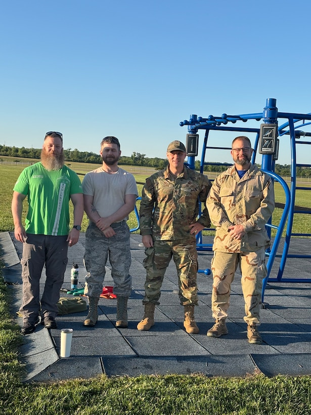 A group of men wearing military and civilian attire stand near an obstacle course