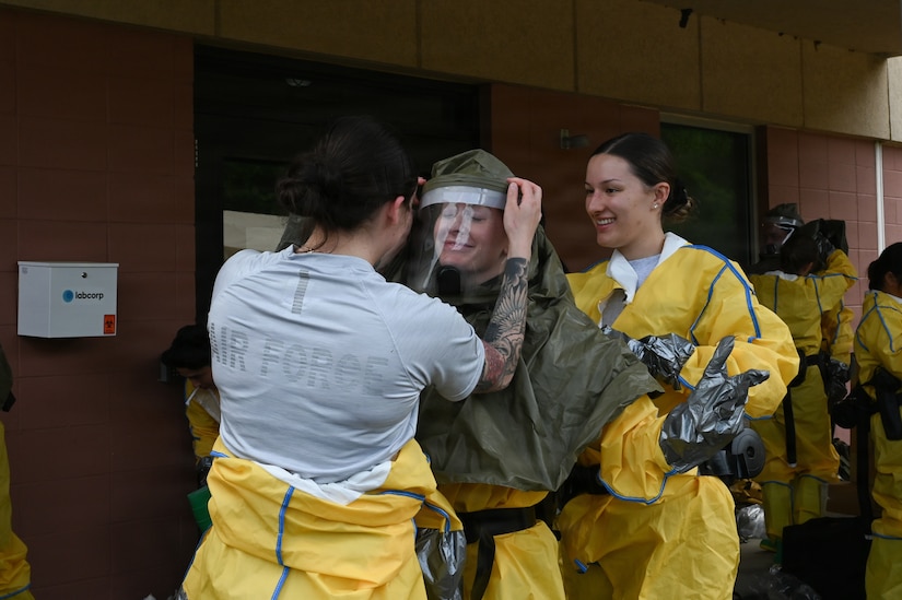 Three women help each other put on hazmat protective clothing and gear.
