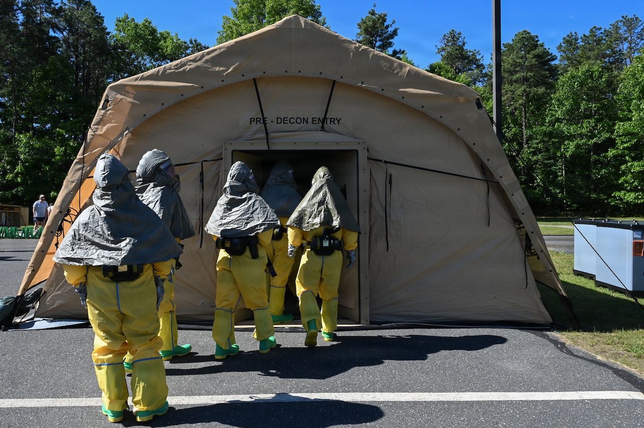 Four people wearing hazmat gear enter a tent.