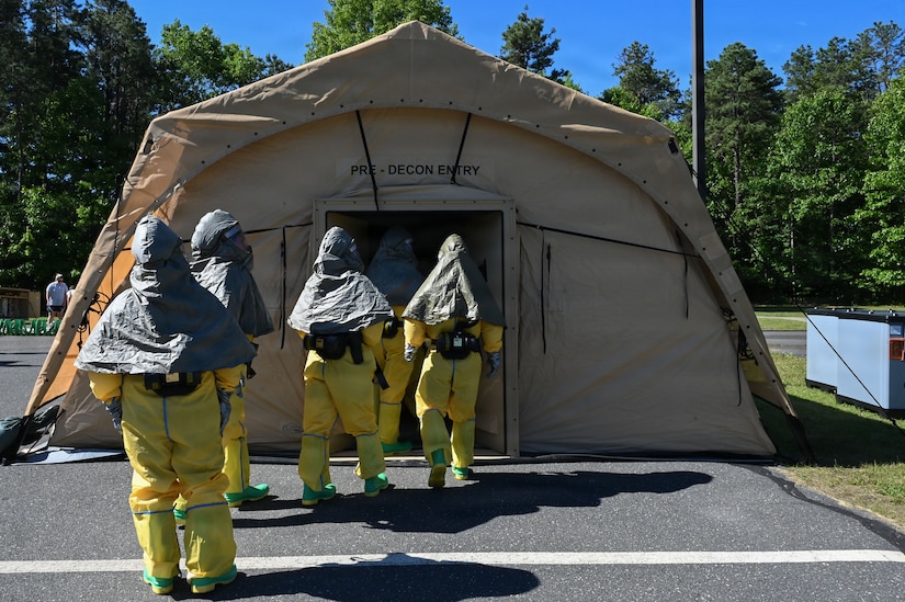 Four people wearing hazmat gear enter a tent.