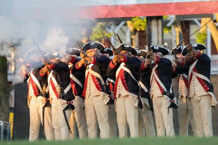 Army Soldiers dressed in Revolutionary War-era uniforms are firing from ceremonial rifles during a demonstration at an outdoor show.