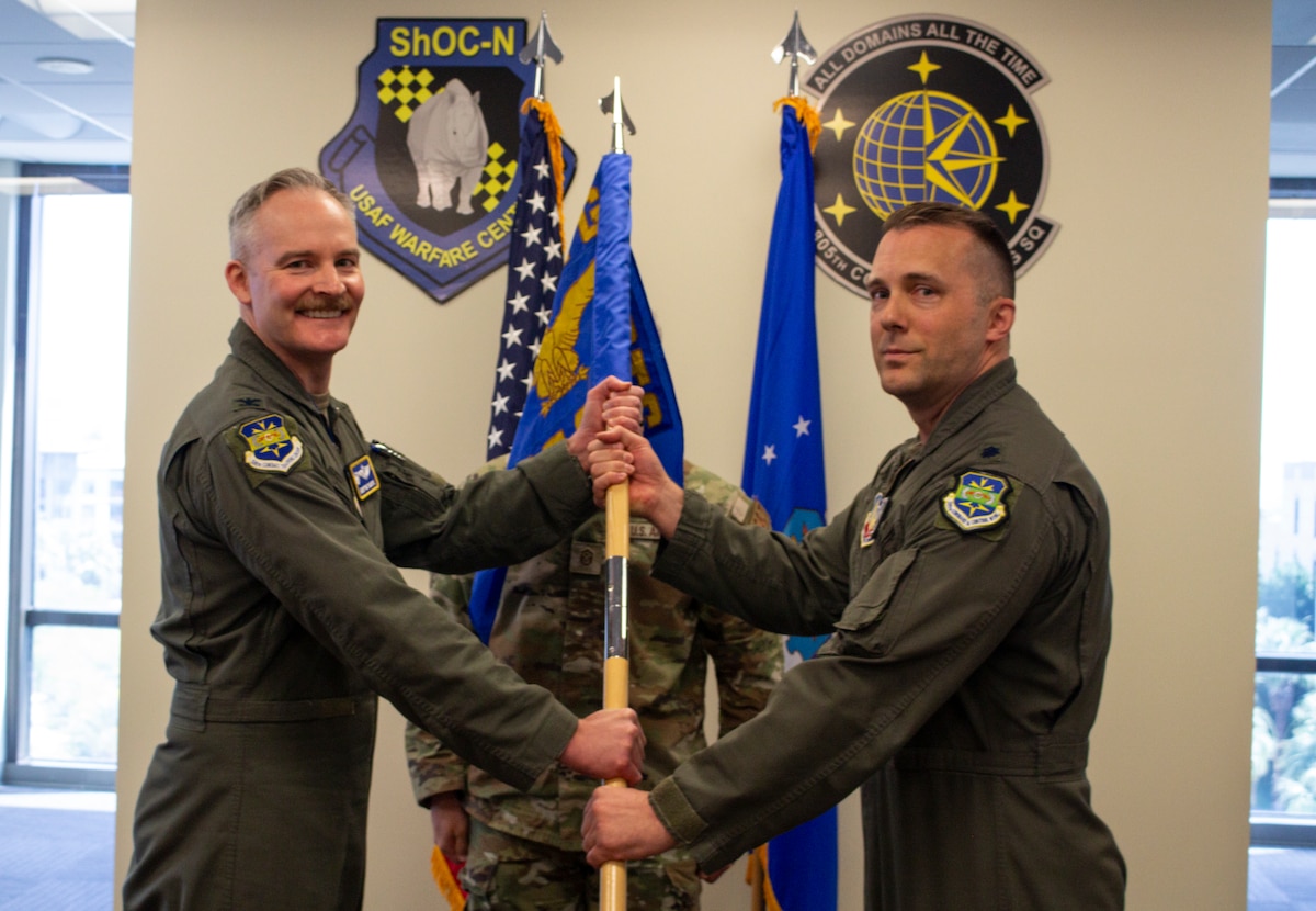 two US Airmen hold a unit guidon flag in between them