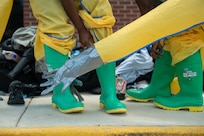 Airmen put on bright green boots and yellow hazmat gear.