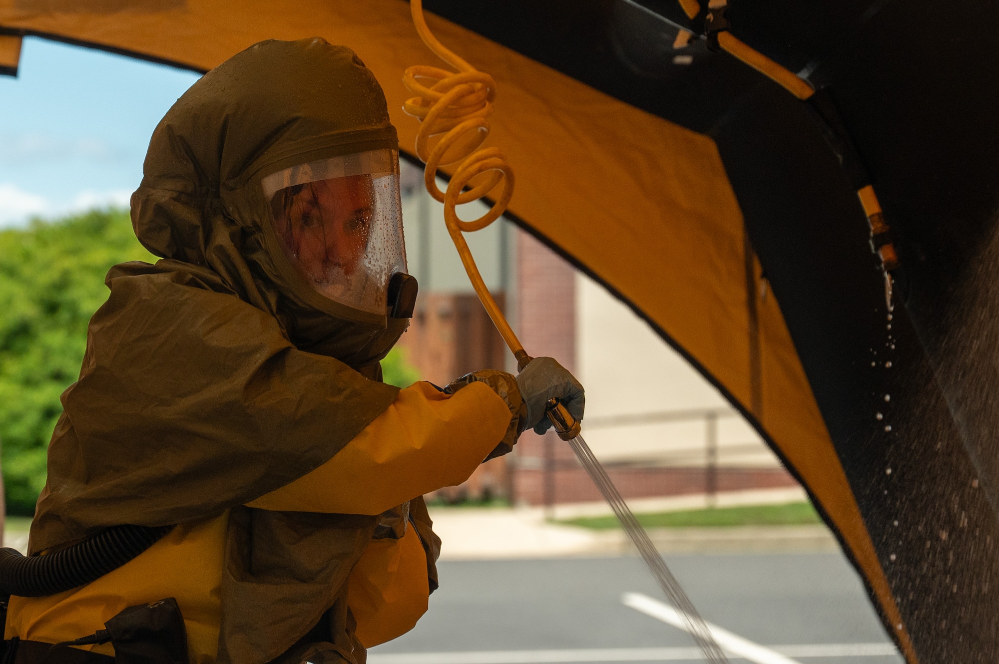An airman wearing hazmat gear holds a long tube.