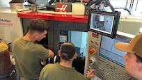(CAMP PENDLETON, Calif.) – Marines assigned to 1st Maintenance Battalion observe a machining operation on the Advanced Integrated Mobile Machine Shop (AIMMS) hHybrid sSystem alongside Naval Surface Warfare Center, Carderock Division engineer Ryan Smith during New Equipment Training (NET) at Camp Pendleton, California. The hybrid system combines additive and subtractive manufacturing capabilities, enabling Marines to fabricate and repair metal components in operational environments rather than relying solely on traditional supply chains.