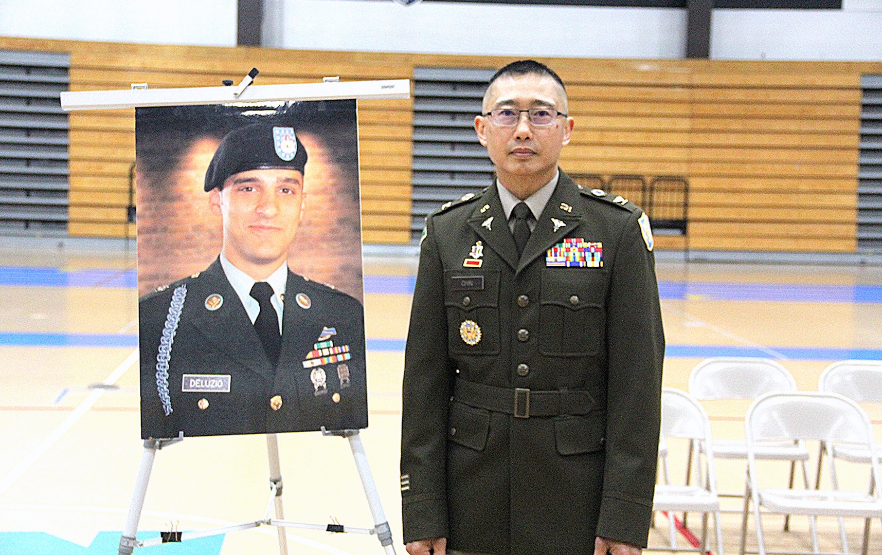 A man wearing an Army uniform stands beside a photo