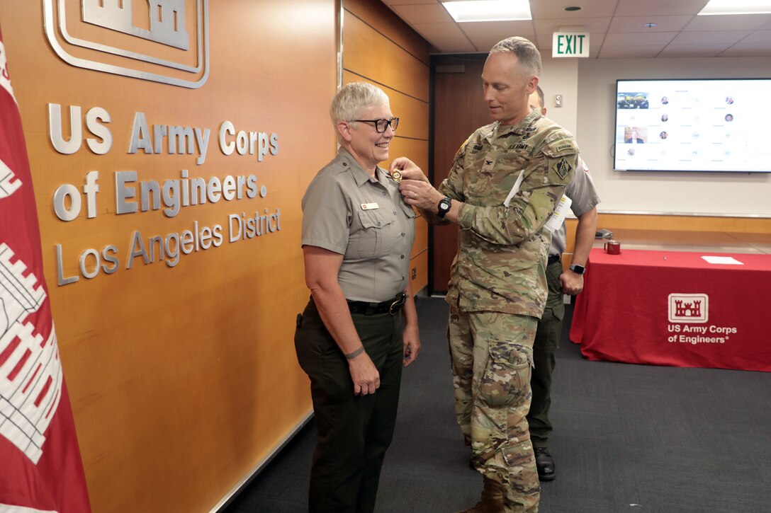 Col. Andrew Baker, USACE LA District commander, pins a park ranger badge onto USACE LA District Park Ranger Marlene Schmitt’s uniform during a pinning ceremony June 3 at the USACE LA District headquarters building.