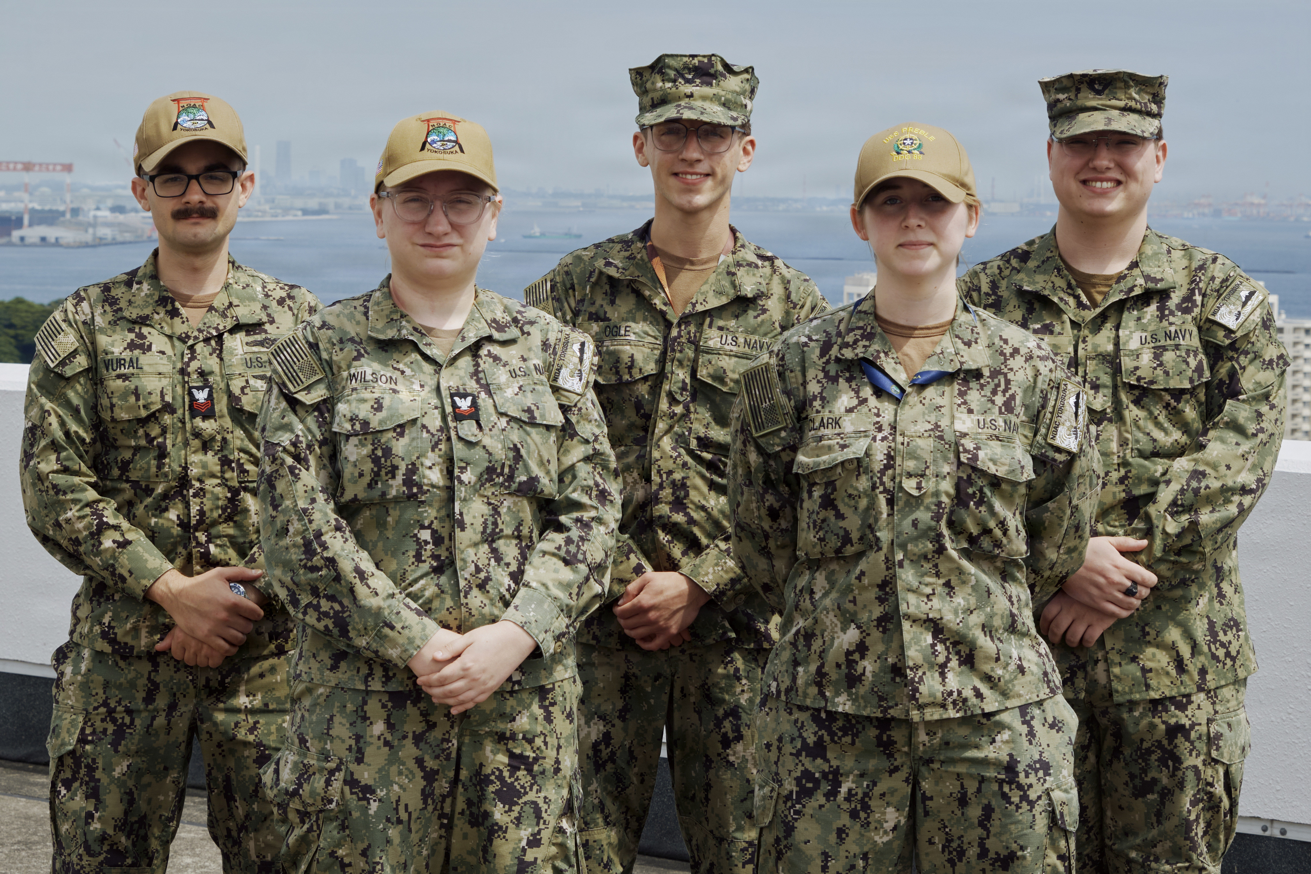 (Front row from left to right) Aerographer's Mate 2nd Class Celestial Wilson, Airman Sara Clark, (second row from left to right) Aerographer's Mate 1st Class Batuhan Vural, Airman Recruit Corey Ogle, and Airman Andie Miller all of Naval Oceanography Anti-Submarine Warfare Center (NOAC) Yokosuka pose on top of the command's local headquarters with Tokyo Bay in the background May 27, 2026. The NOAC Yokosuka team tracks the weather to protect Fleet Activities Yokosuka Sailors, military families, and the places they live and work while serving as a critical resource for asset protection and risk management for Commander, U.S. Naval Forces Japan/Region Japan (CNFJ/RJ) ashore forces and U.S. 7th Fleet afloat personnel and ships.
