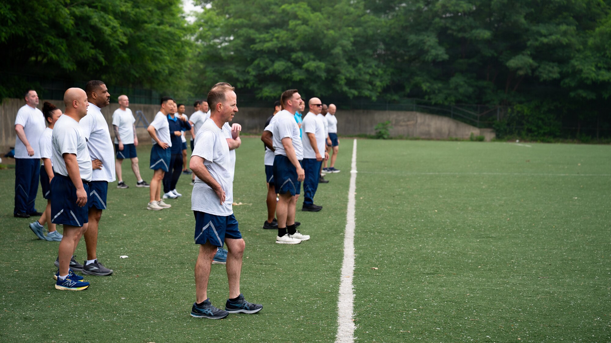 A group of PT uniformed personnel are waiting behind a line on a field