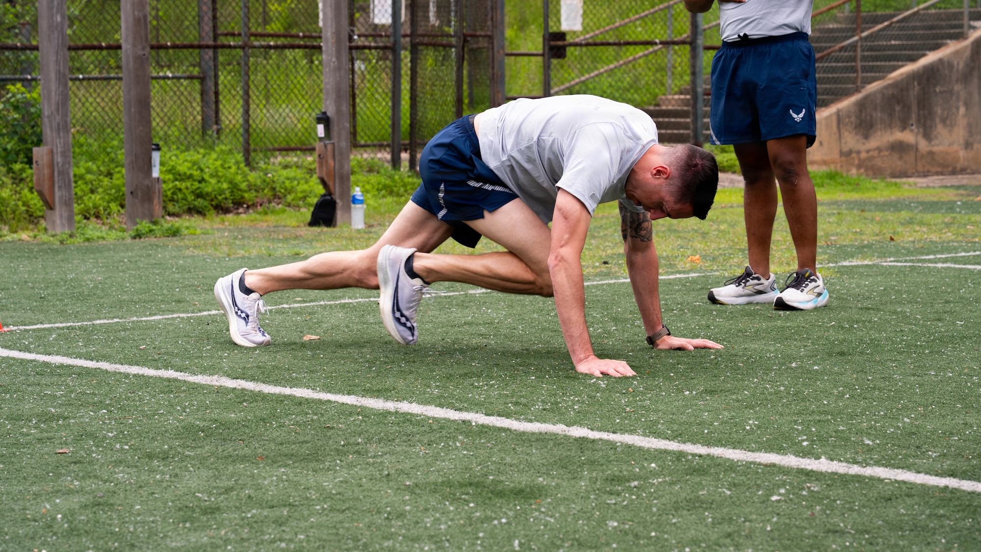 A man in a military PT uniform is doing a mountain climber exercises which involves both hands on the ground with arms fully extended and driving knees up, one at a time