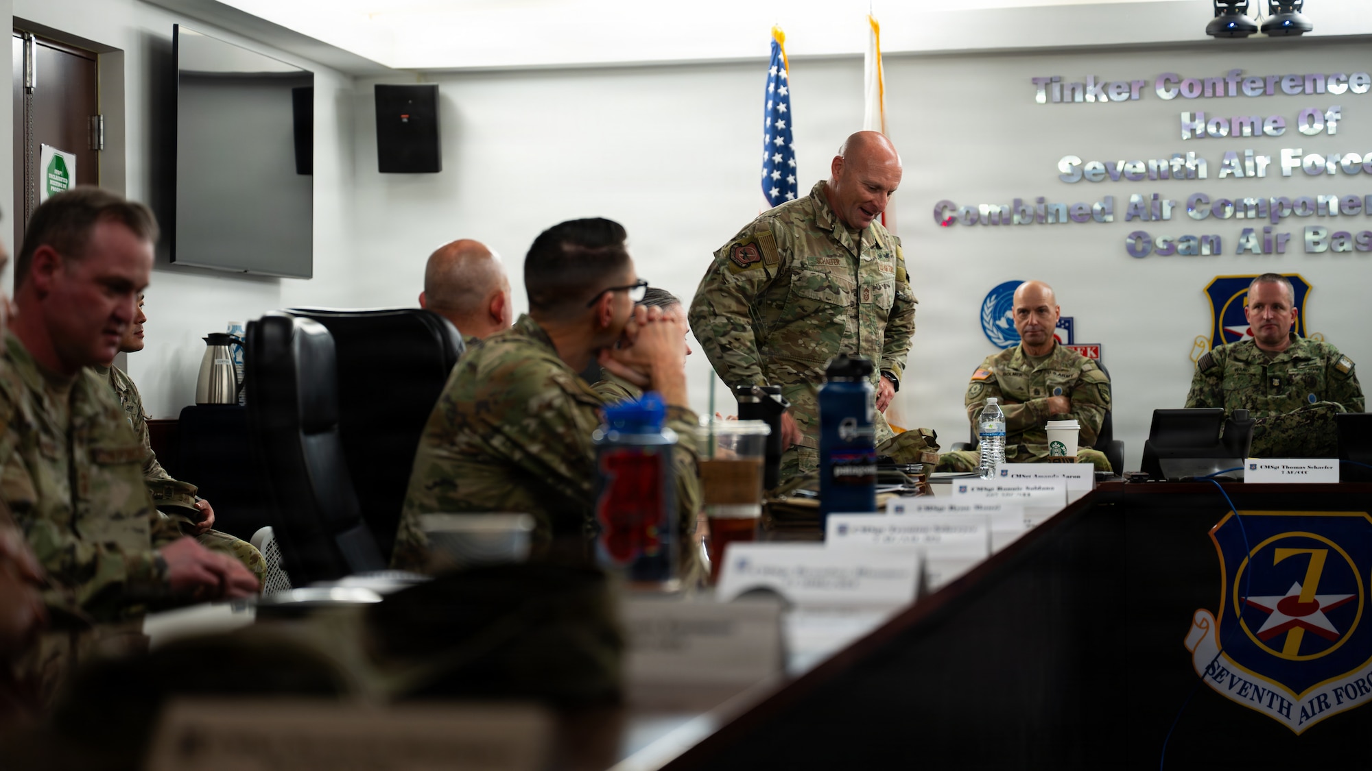 A group of uniformed personnel sit around a U shaped table in a conference room