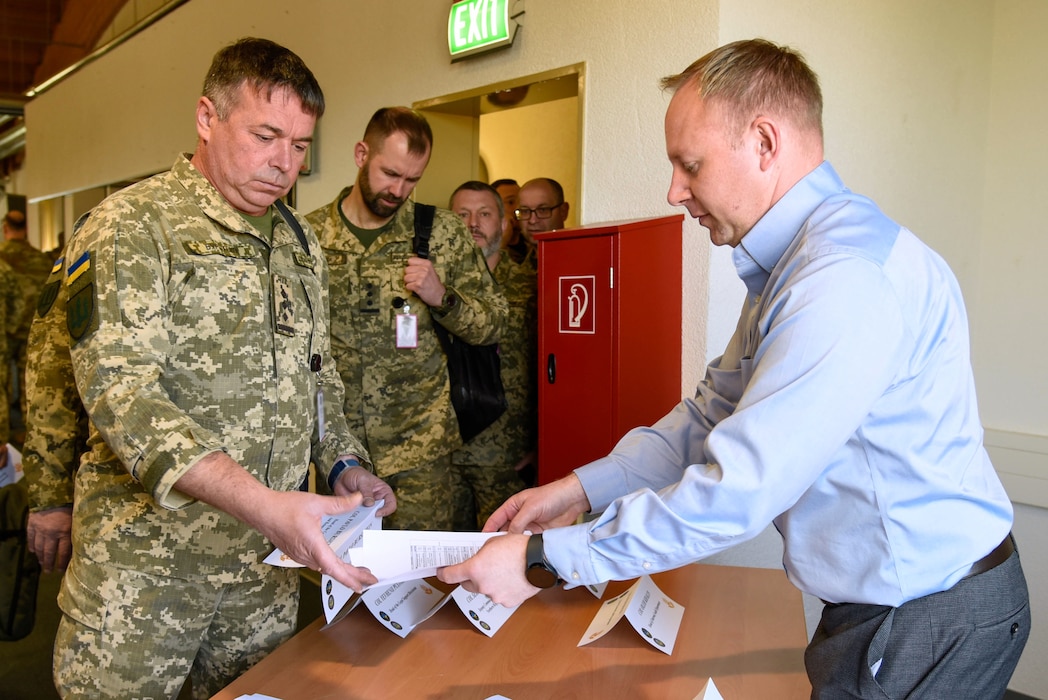 a man in a blue shirt hands a packet of papers to a man in a military uniform