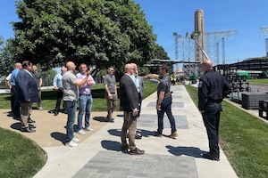 Men wearing casual attire stand in a group outdoors while talking. Two are gesturing.